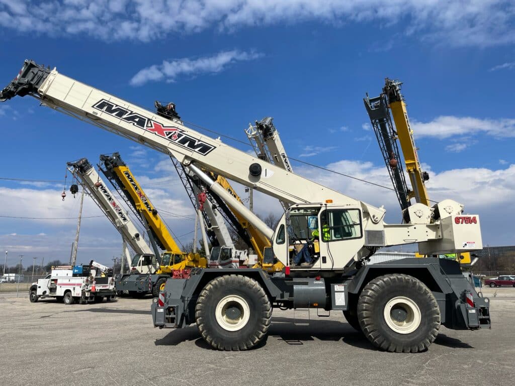 A rough terrain crane sitting in a lot with other cranes