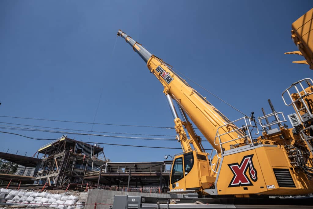 Yellow construction crane lifting materials against a clear blue sky at a job site.