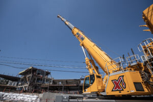 Yellow construction crane lifting materials against a clear blue sky at a job site.