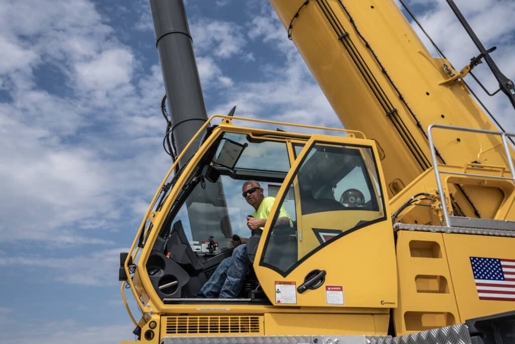 Crane operator in yellow cabin controlling heavy machinery against a cloudy sky.