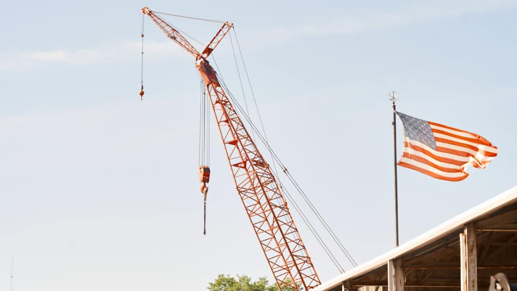 A tower crane in the air with an american flag in the foreground