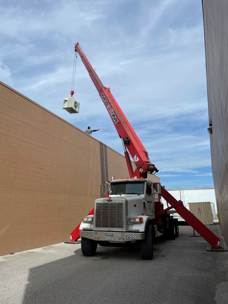 A Maxim crane boom truck working on a lifting project in a tight space between two buildings.