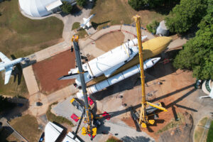 Heavy crane lifting a rocket at an aerospace museum, showcasing space transportation technology.
