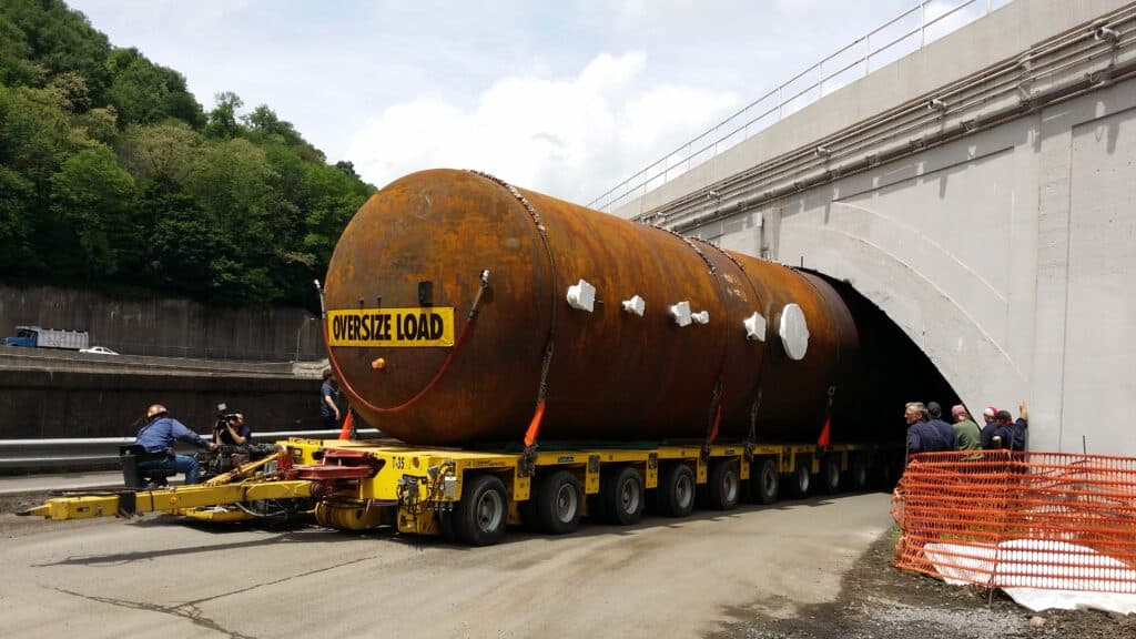 Oversized load transportation navigating through a tunnel with workers and equipment.