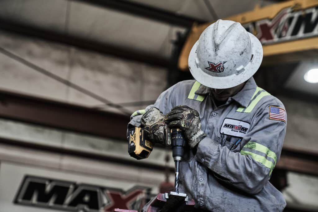 Worker using a power drill to drill metal in a construction environment.