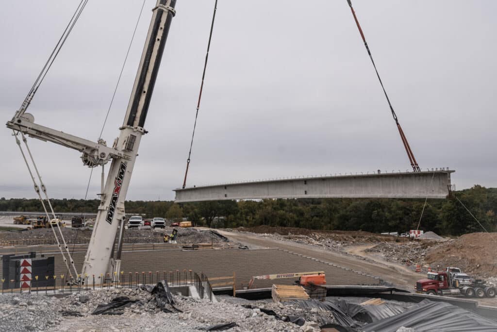 Mobile crane lifting a concrete bridge segment at a construction site.