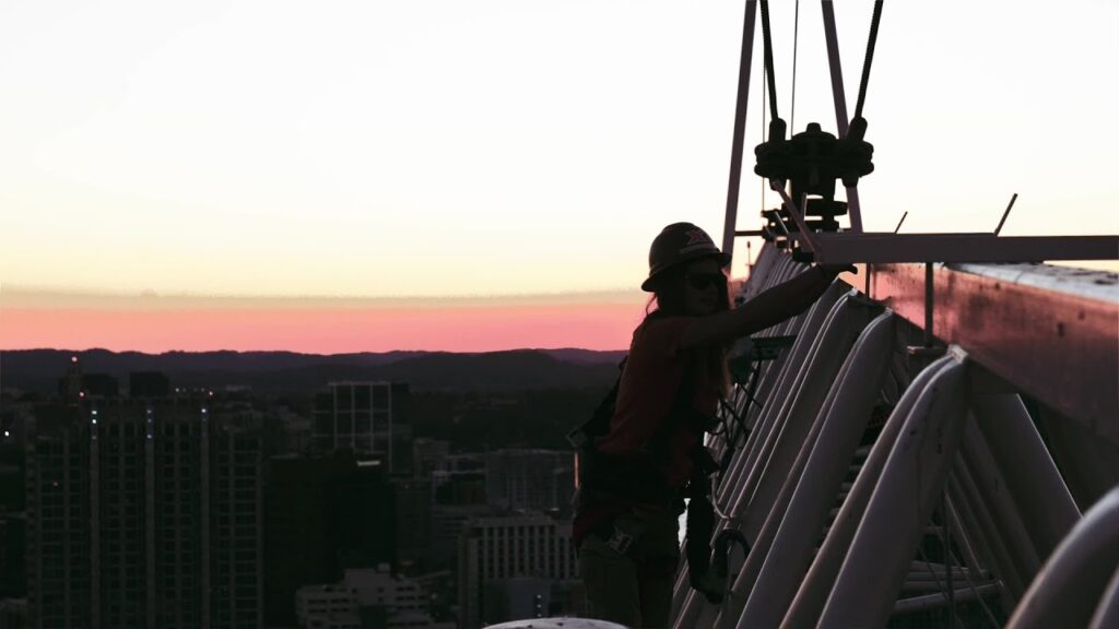 Worker on rooftop at sunset, showcasing construction and city skyline.