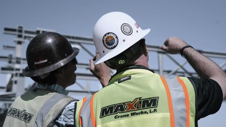 Maxim Crane team discussing work at a job site under bright blue skies.