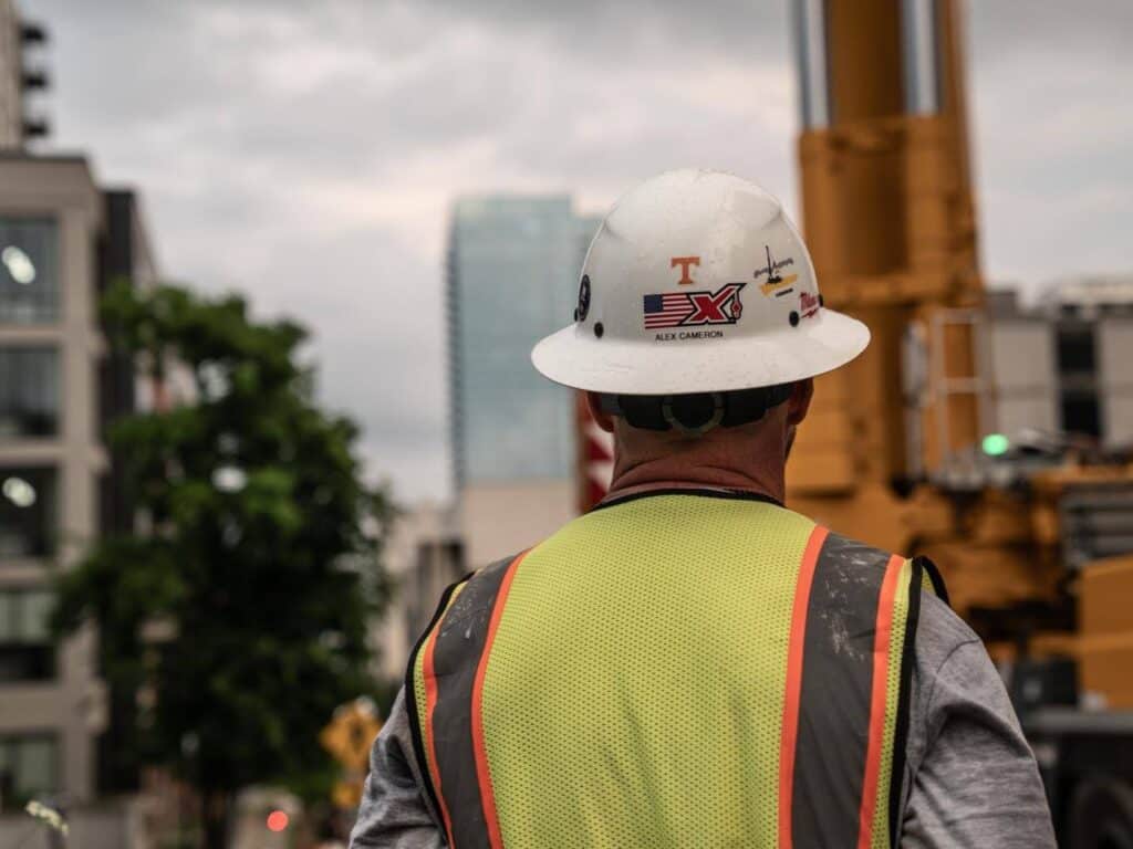 Construction worker in safety gear oversees a building project against a city backdrop.