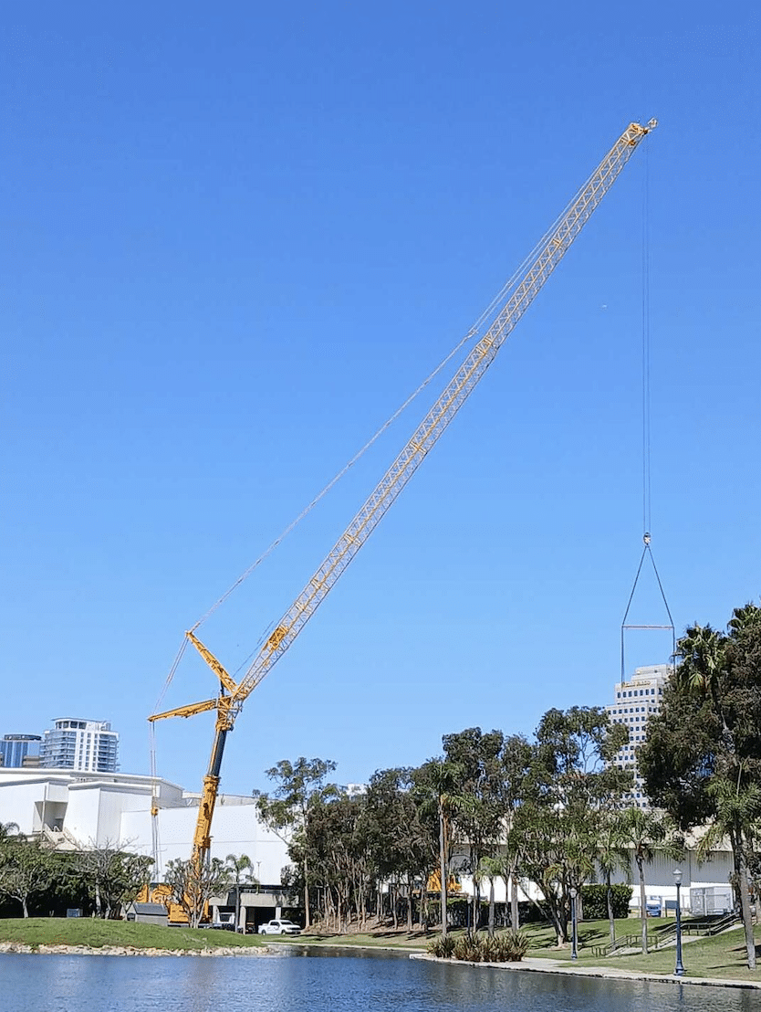 Heavy construction crane lifting materials by the water under a clear blue sky.
