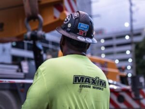 Maxim Crane Works worker in safety gear operating crane at construction site.