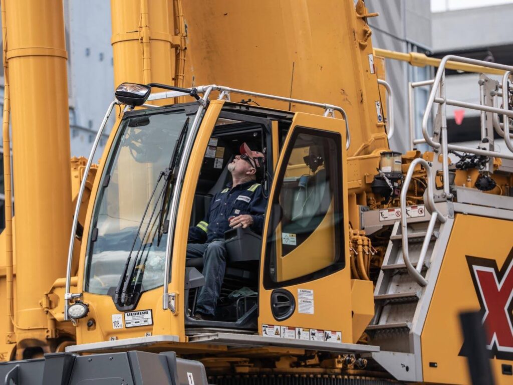 Crane operator in cabin, managing heavy machinery at construction site.