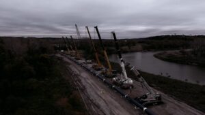 Cranes installing a pipeline along the Platte River in cloudy conditions.