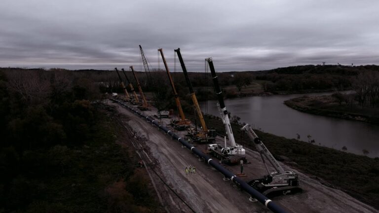 Cranes installing a pipeline along the Platte River in cloudy conditions.