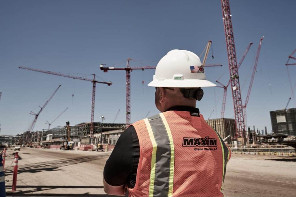 Worker monitoring construction site with cranes, ensuring safety and project execution.