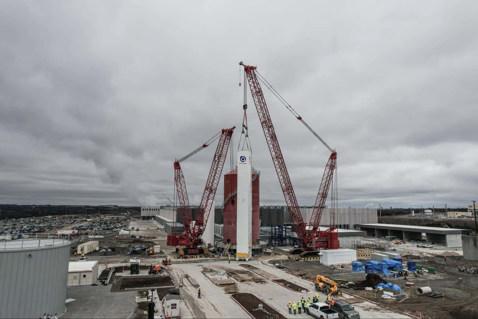 Heavy cranes work efficiently at a construction site under overcast skies.