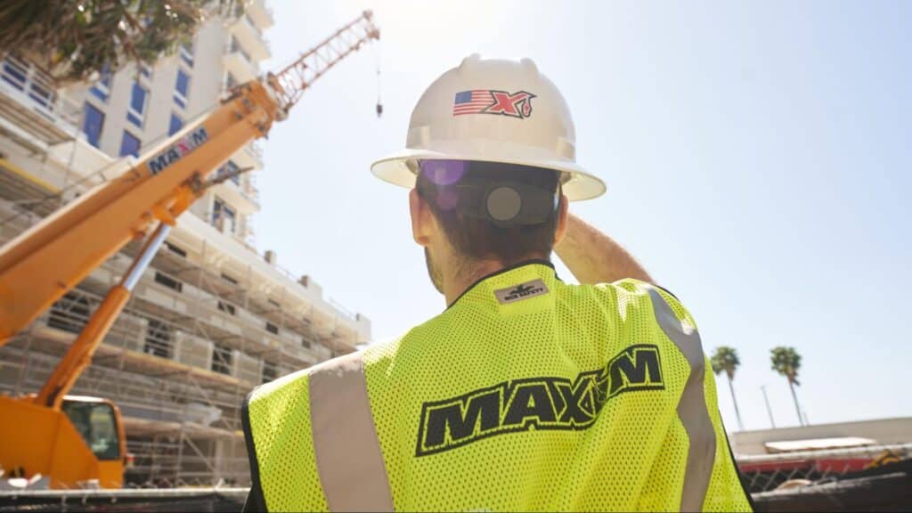 Maxim crane operator supervising construction site activities under clear blue skies.