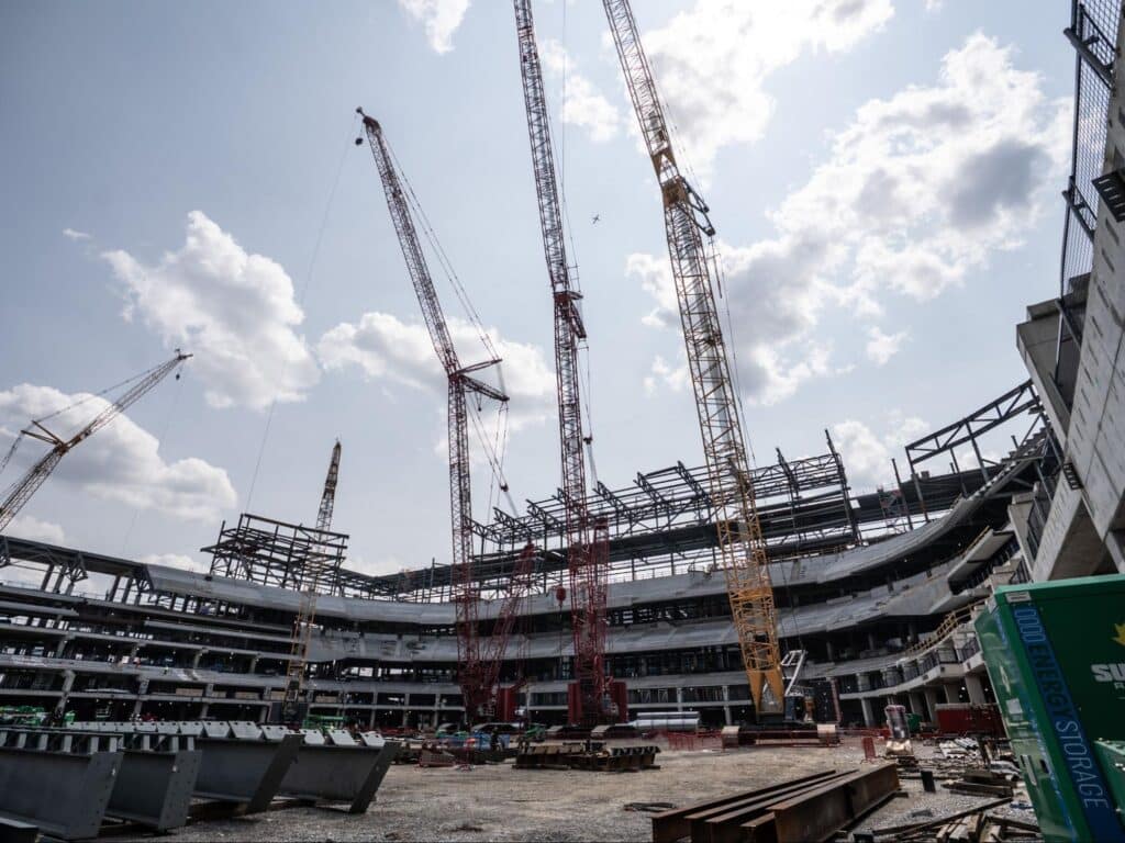 Stadium construction site bustling with cranes and progress under bright skies.