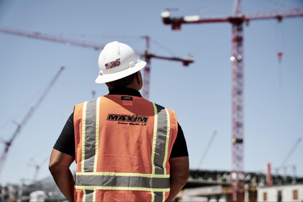 Maxim crane worker supervising construction site with cranes and clear skies.