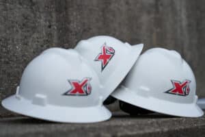Three white hard hats with maxim logos positioned on a concrete surface.