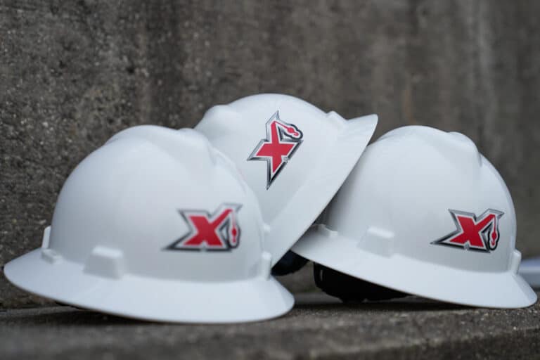Three white hard hats with maxim logos positioned on a concrete surface.