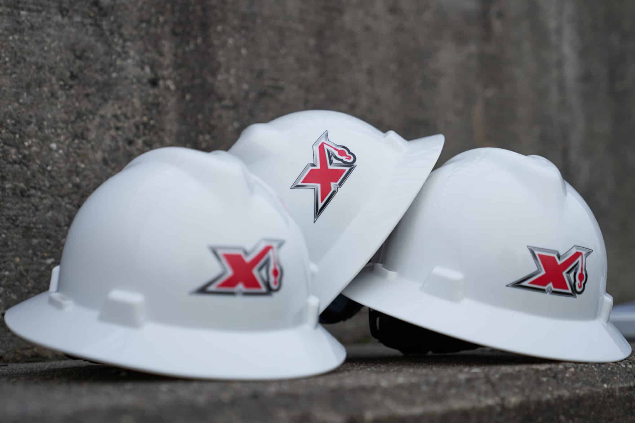 Three white hard hats with maxim logos positioned on a concrete surface.
