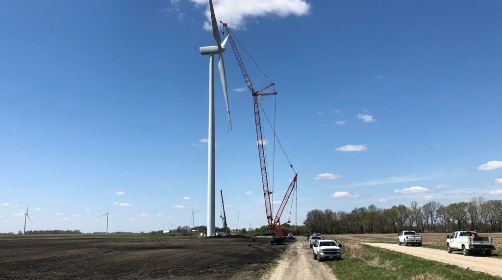 Wind turbine assembly in progress under a bright blue sky.