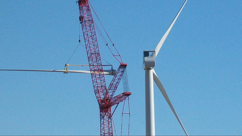 Cranes lifting wind turbines against a clear blue sky.