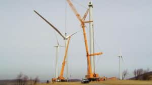 Wind turbines being assembled with cranes in a renewable energy site.