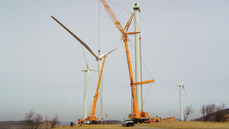 Wind turbines being assembled with cranes in a renewable energy site.