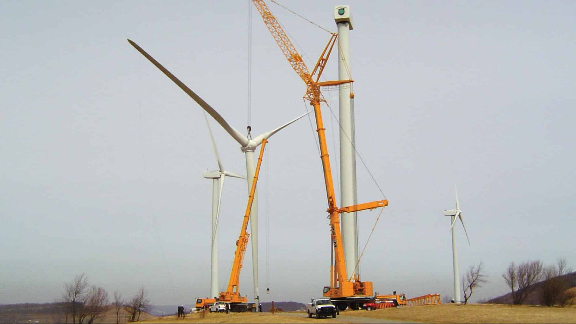 Wind turbines being assembled with cranes in a renewable energy site.