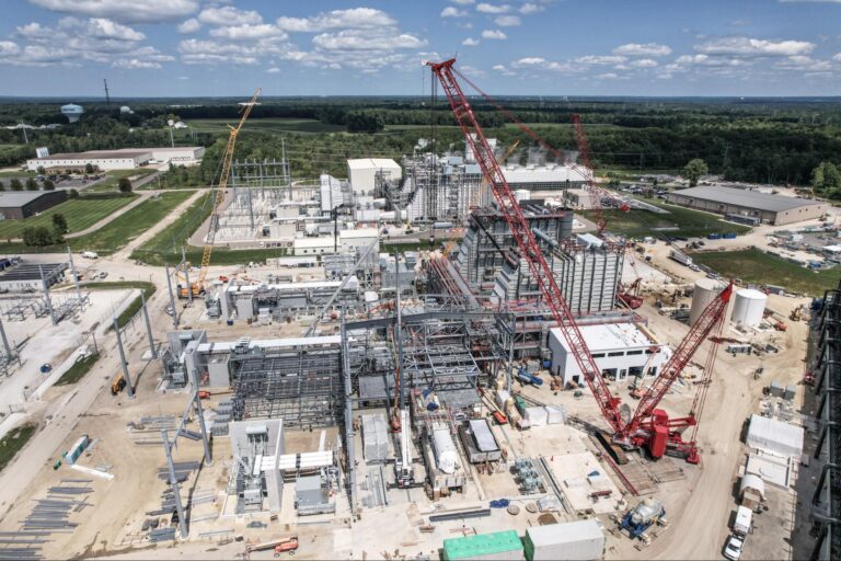 Cranes operating at a busy construction site under a bright blue sky.