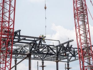 Workers installing steel beams at a construction site under a clear blue sky.