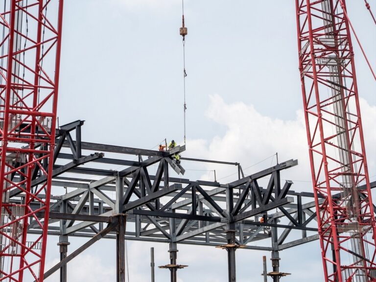 Workers installing steel beams at a construction site under a clear blue sky.