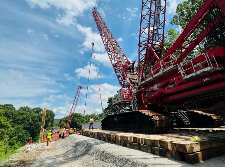 Cranes lifting materials at a construction site under a bright blue sky.