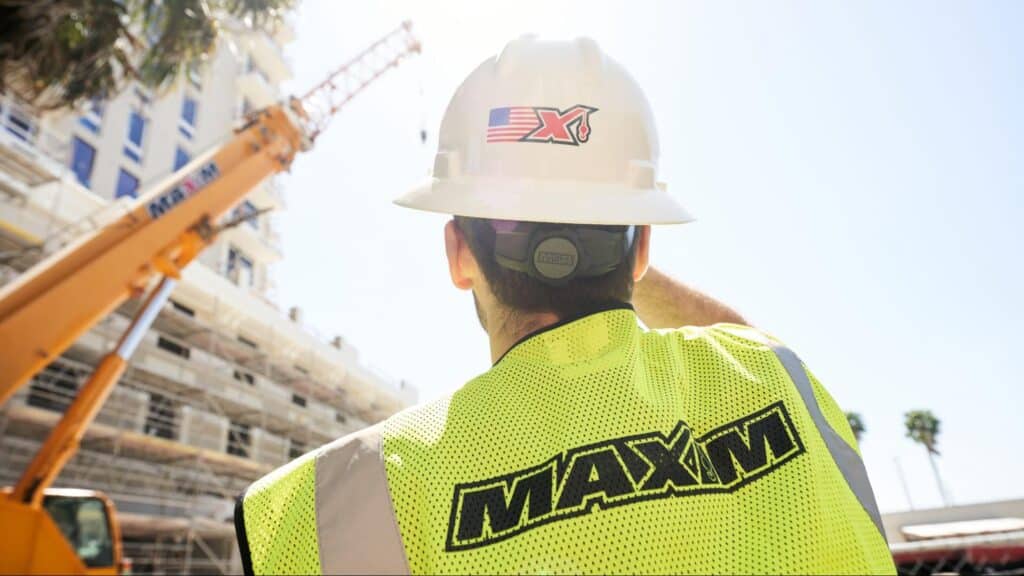 Maxim employee in safety gear supervising a construction project under clear skies.