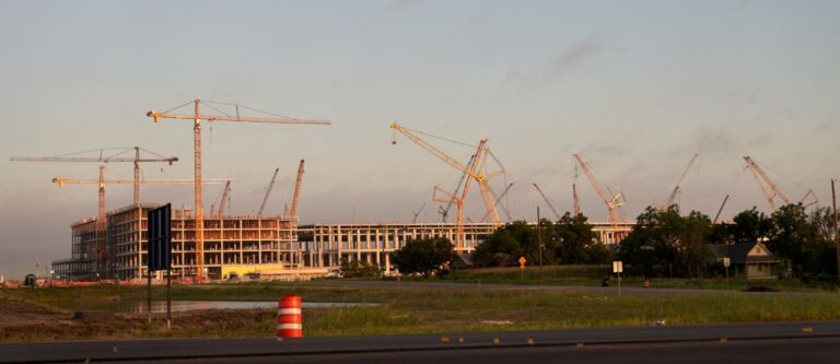 Cranes and new buildings under construction at sunset against a clear sky.