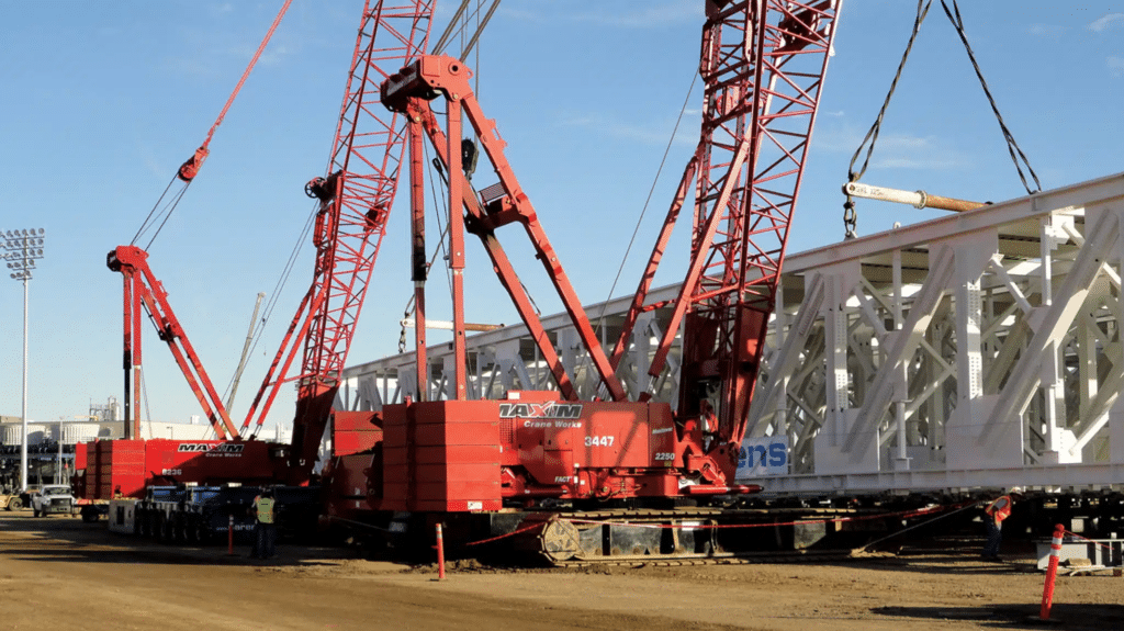 Cranes lifting heavy structures at a bustling construction site.