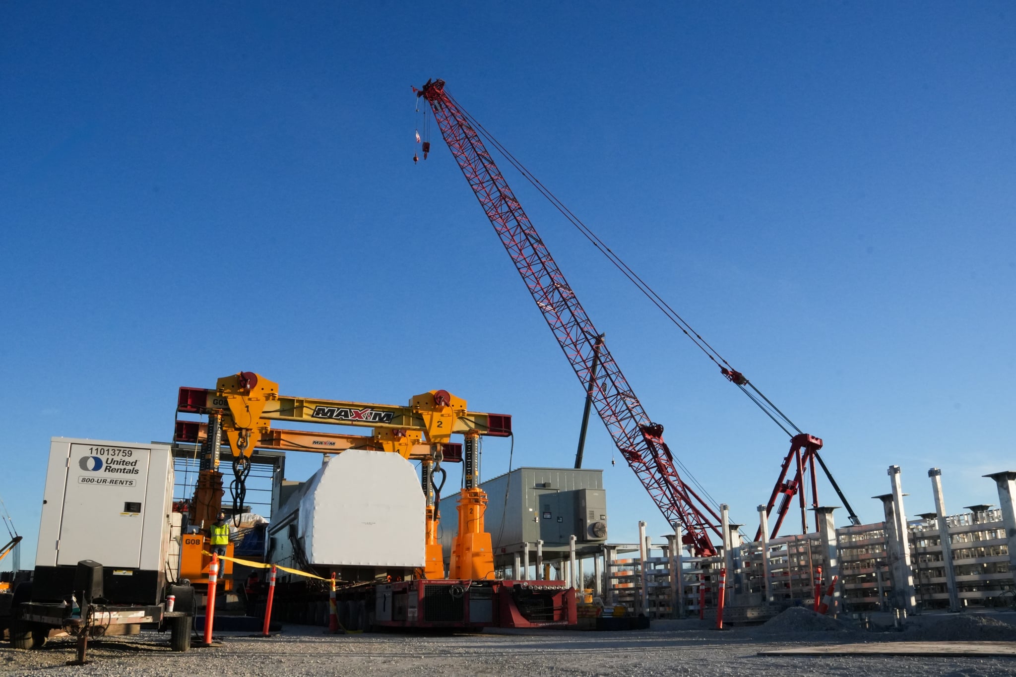 Large construction crane lifting materials at a busy construction site under clear blue skies.