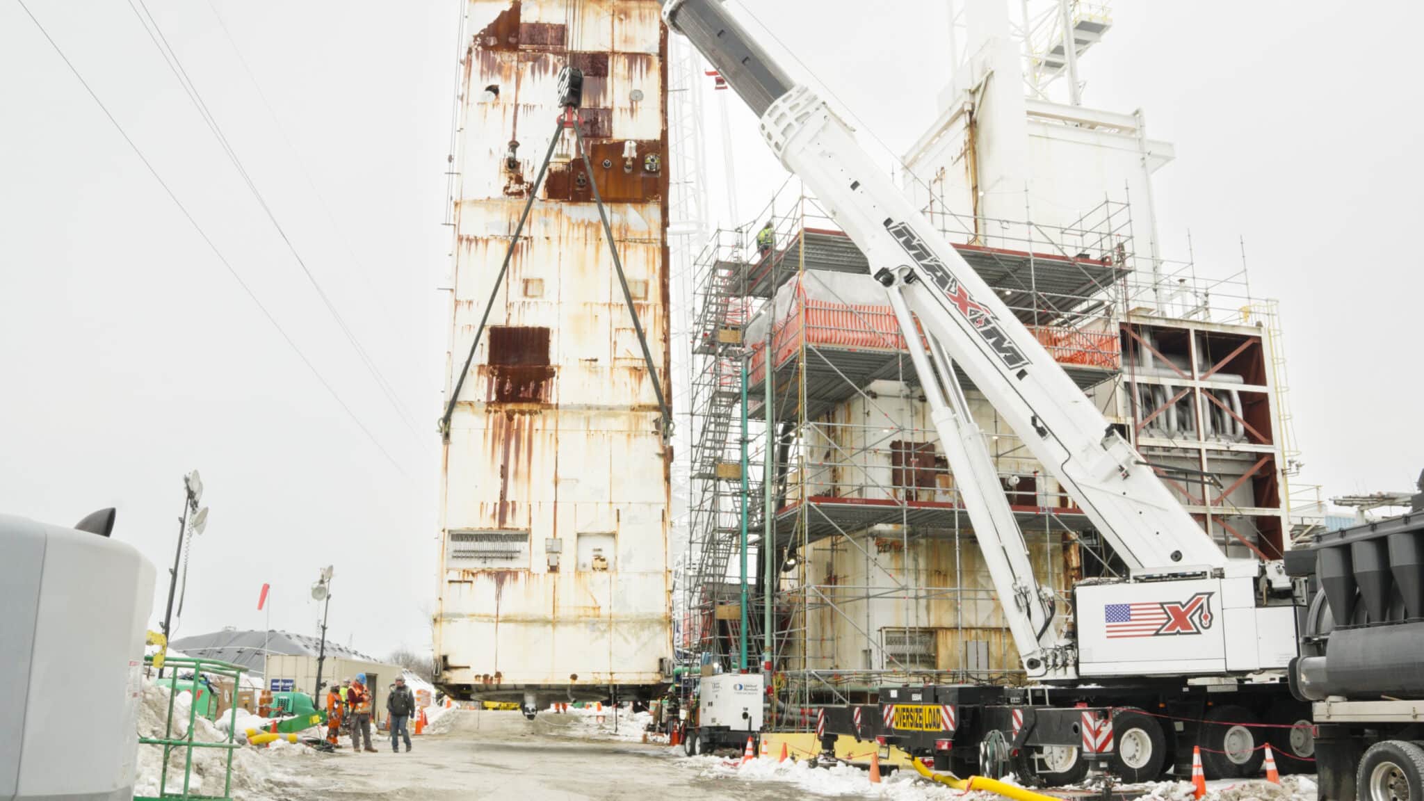 Crane operation at a construction site with scaffolding and workers during cold weather.