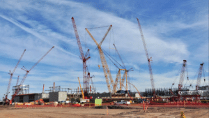 Cranes at a construction site lifting materials against a blue sky backdrop.