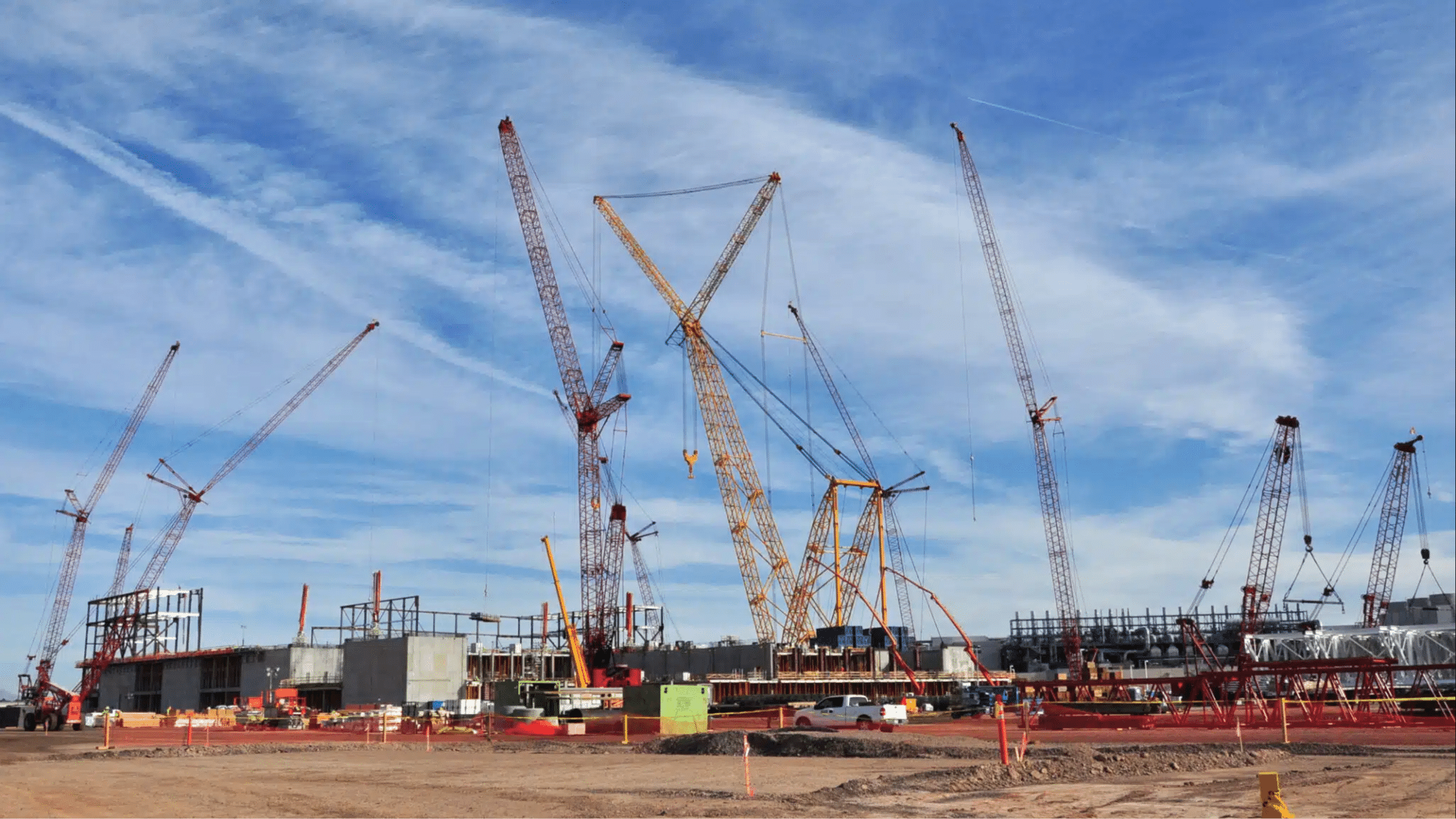 Cranes at a construction site lifting materials against a blue sky backdrop.