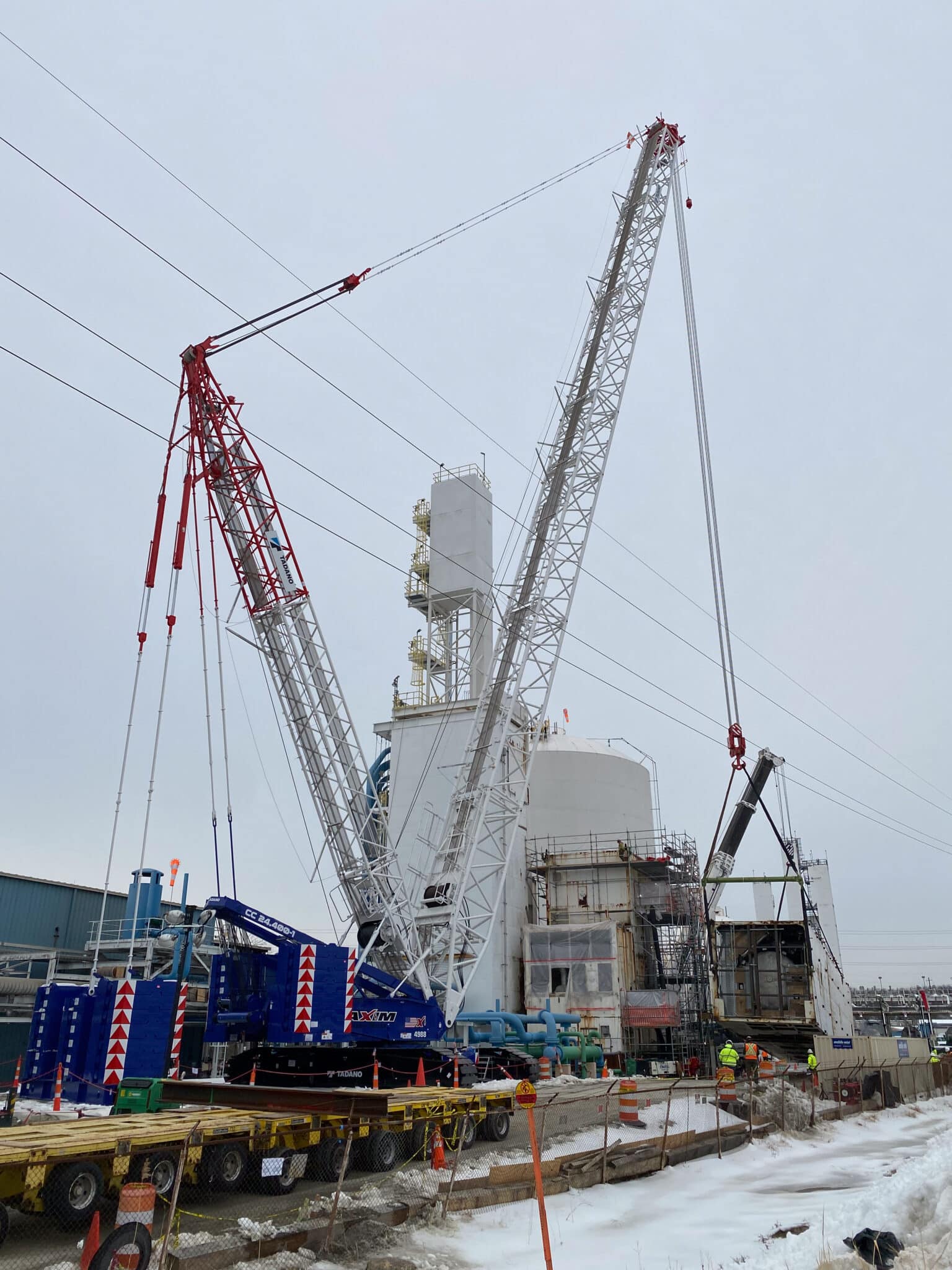 Cranes lifting materials at a construction site under cloudy skies.