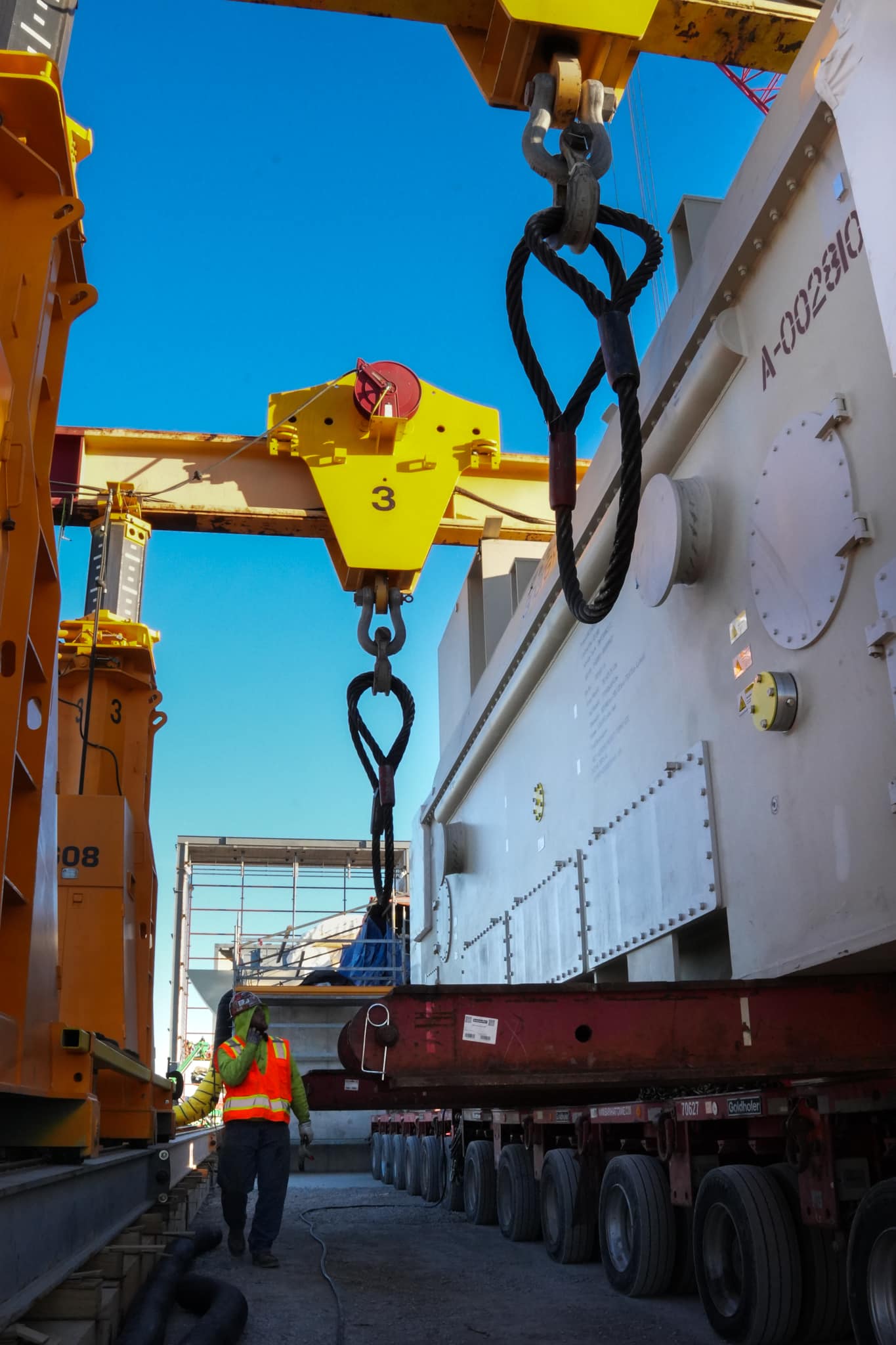 Loading crane lifting heavy equipment at construction site under clear blue sky.