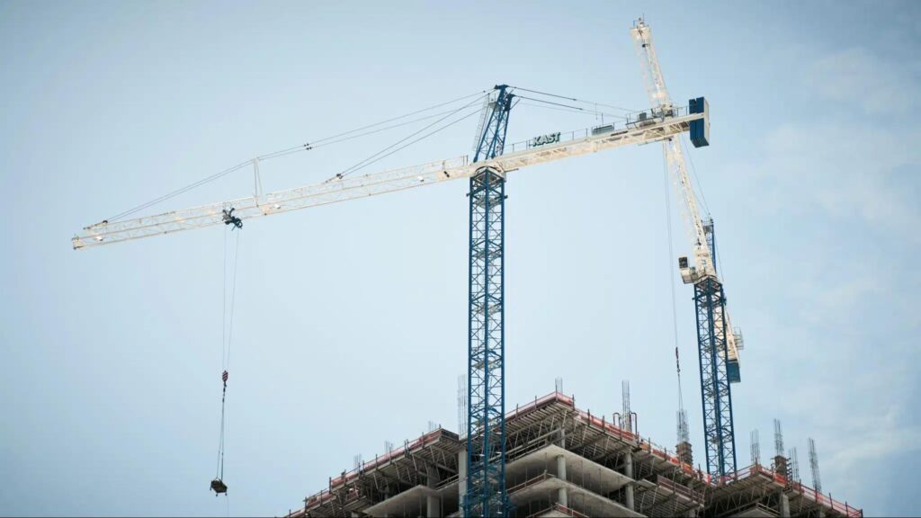 Construction cranes against a blue sky at a building site.