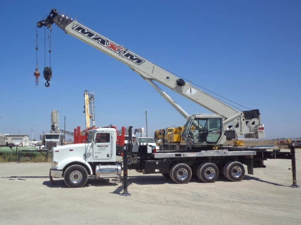 Crane truck lifting equipment at a construction site under a clear blue sky.