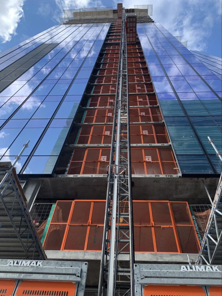 Construction elevator lifting materials to high-rise building with glass facade.
