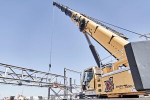 Grove crane lifting steel beams at a construction site under clear blue skies.