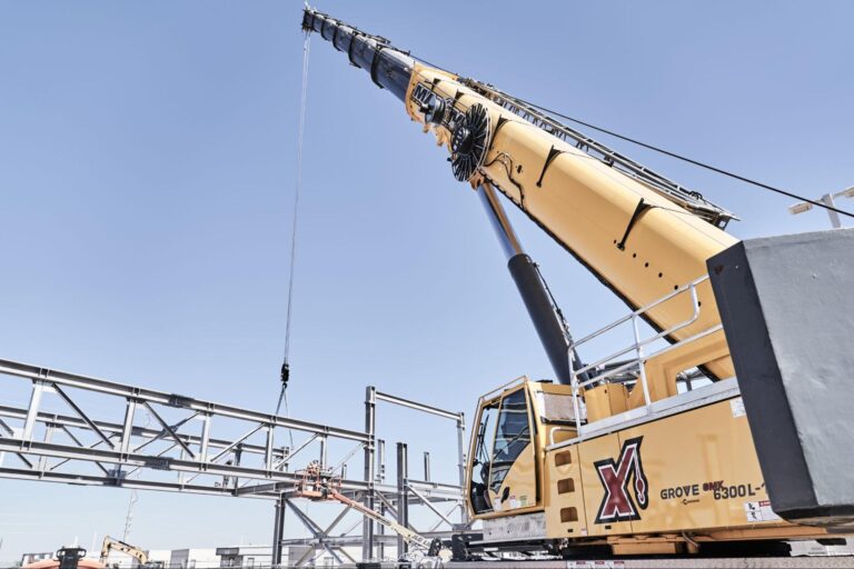 Grove crane lifting steel beams at a construction site under clear blue skies.