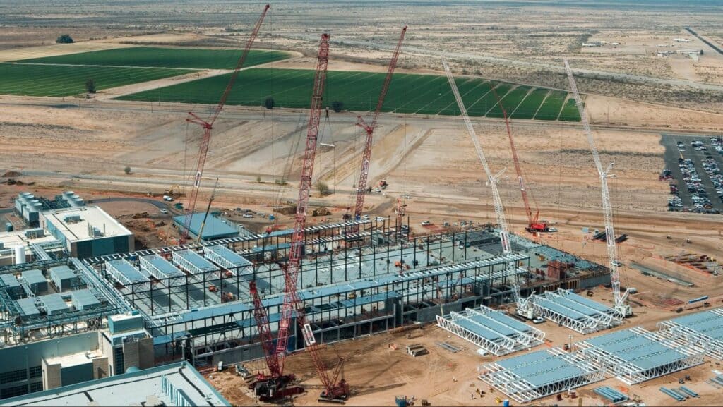 Construction site progress with cranes and structures in a vast desert landscape.